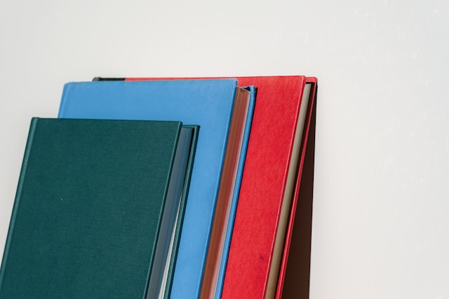 Green, blue, and red books stacked against a white wall.