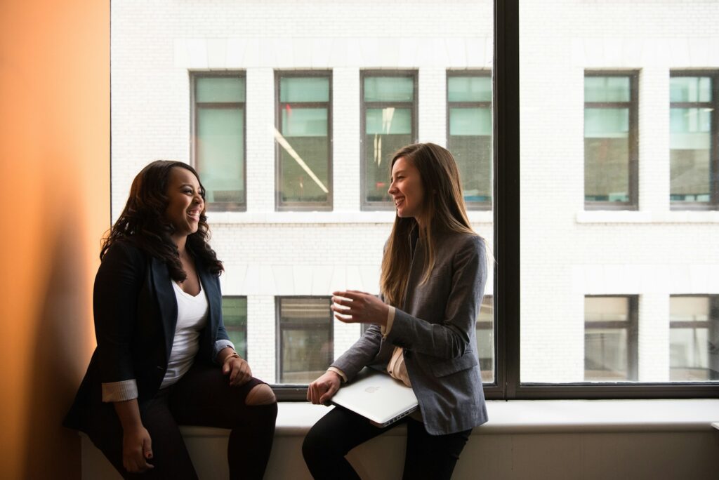 Two women sat on a window sill talking