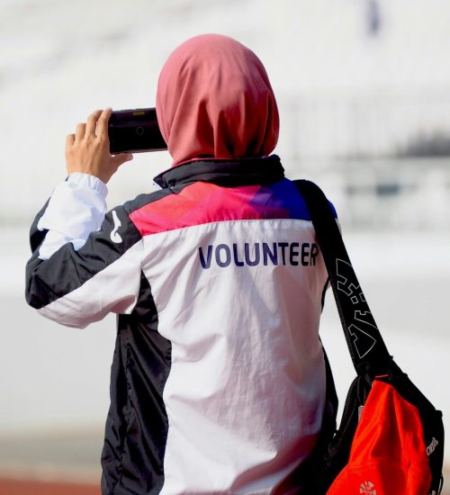 Person holding up a smartphone facing away from the the camera, their jacket reads "volunteer"